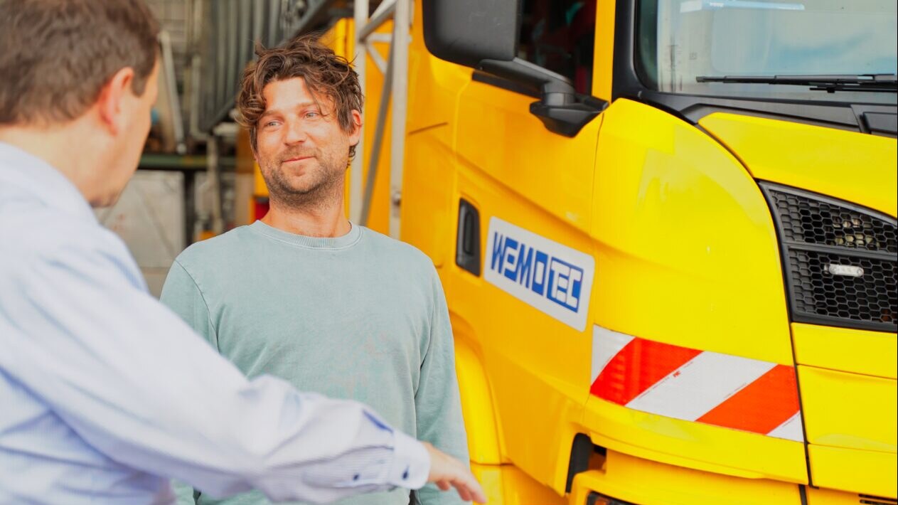 Niklaas Zander vor Ort beim Spediteur: Gespräch mit dem Inhaber vor einem gelben WEMO-tec LKW